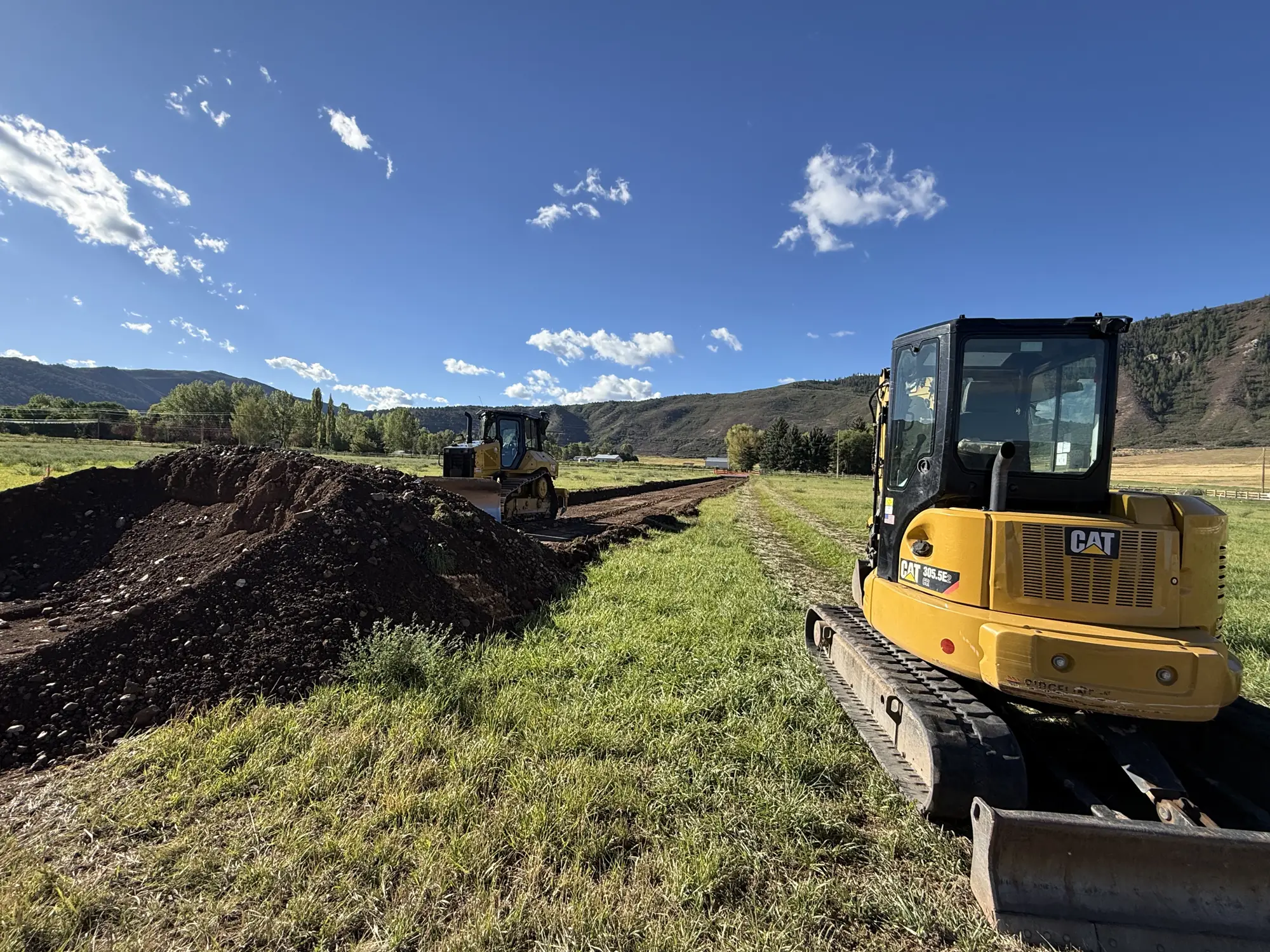 Excavator and dozer working a long grade across an open commercial site