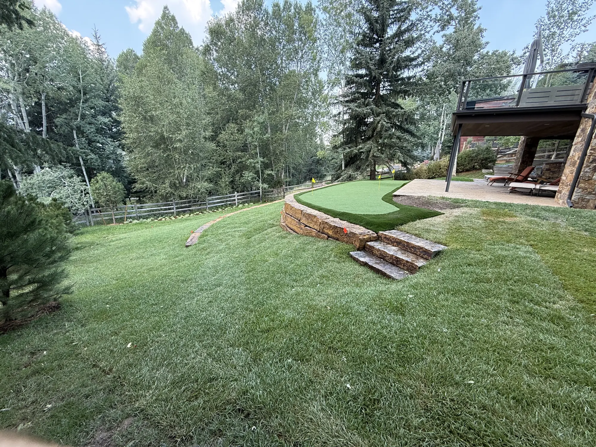 Finished landscape with a putting green, sandstone block wall, stone steps and new lawn at a mountain home