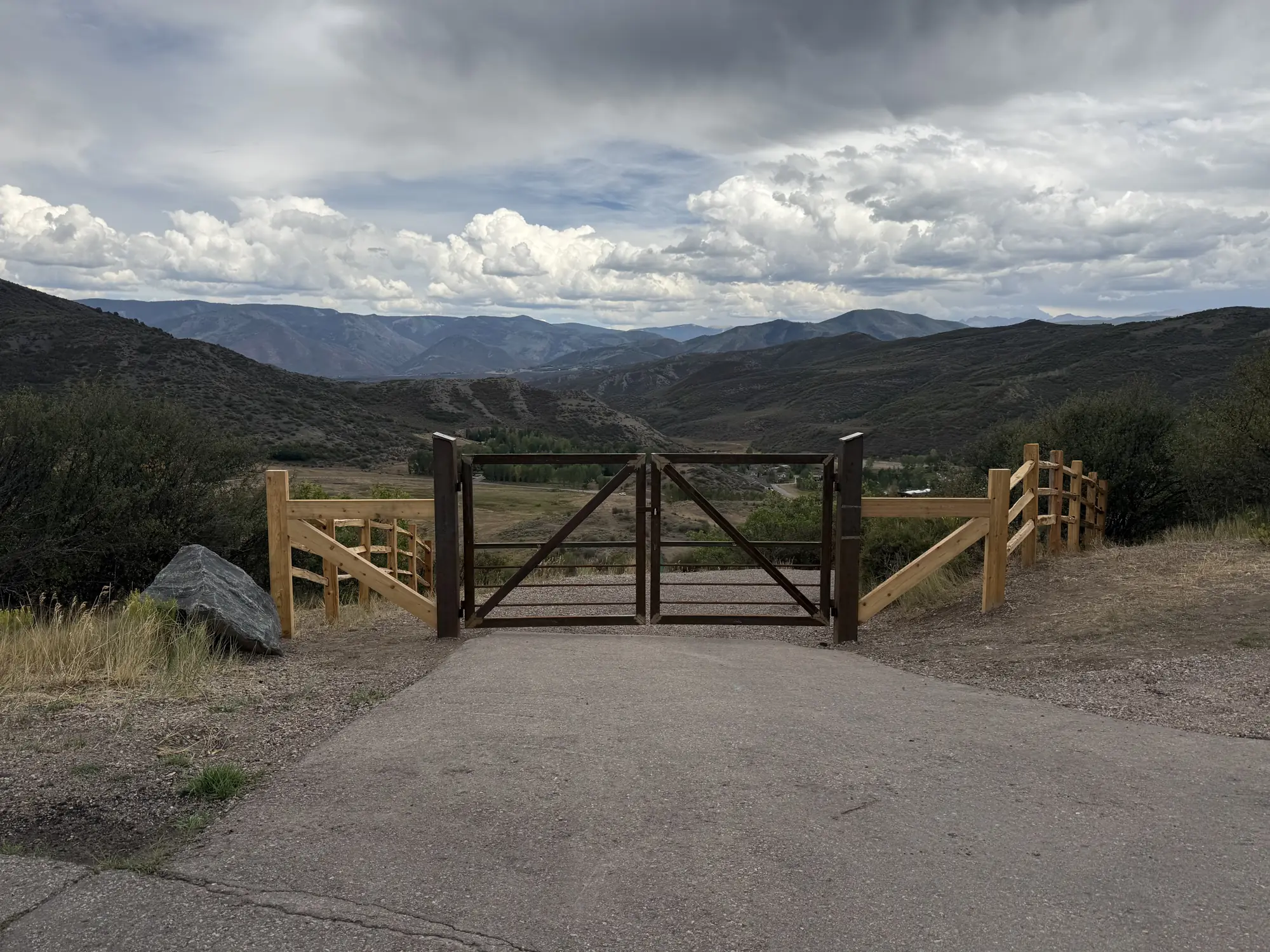 Finished driveway entrance with gate and fencing above a mountain valley